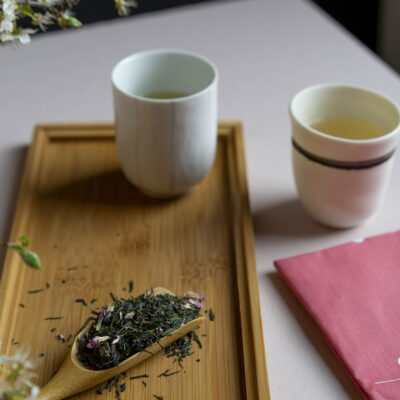 Un cucchiaio di legno con foglie di tè e due tazze di tè caldo