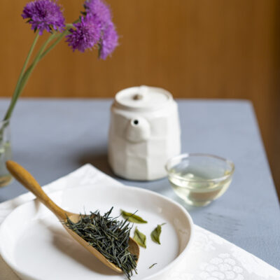 Foglie asciutte sullo sfondo di una teierina bianca e di una tazzina di tè. Ci sono anche tre foglie infuse
